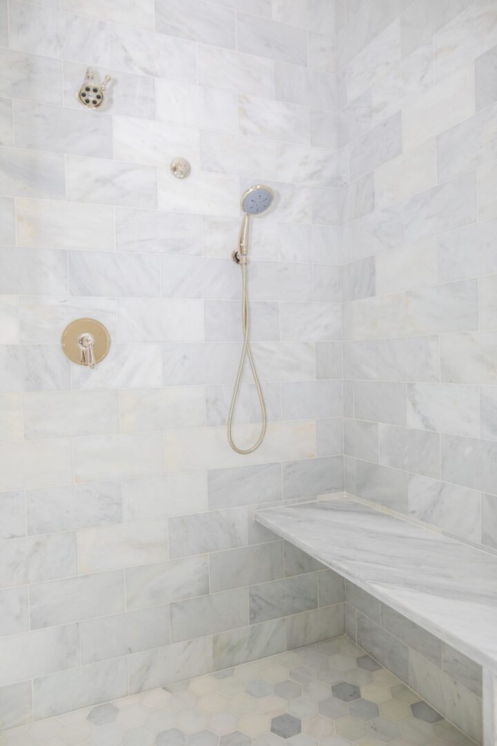 A shower with marble walls and white tile.